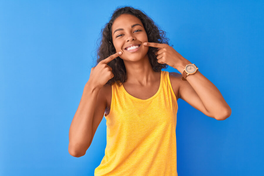 Brunette woman in a yellow tanktop smiles after orthodontic treatment