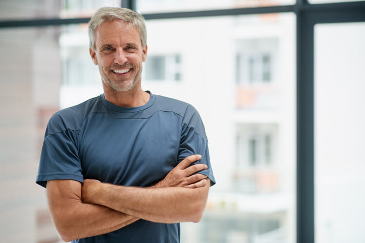 Middle-aged man wearing a gray shirt crosses his arms and smiles after an oral cancer screening