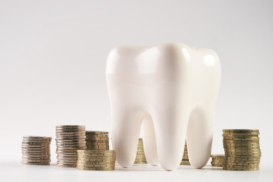 White tooth next to stacks of coins for affordable dental care without insurance