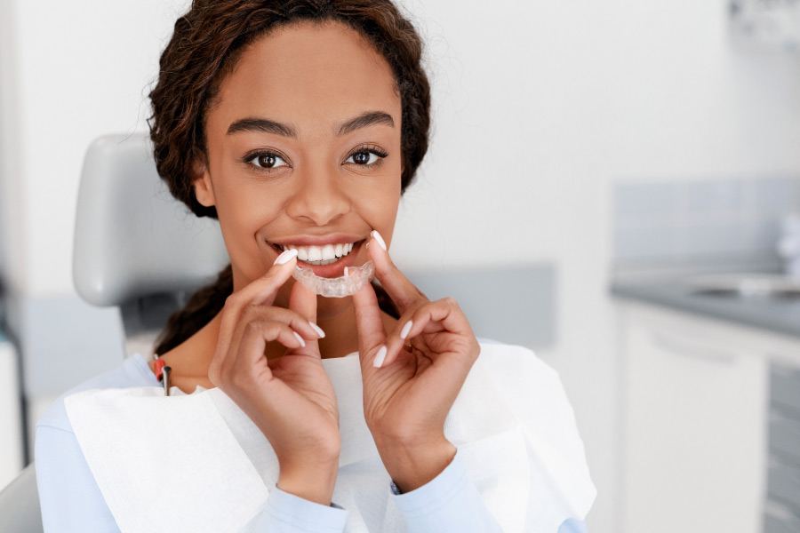 Brunette woman smiles as she puts in her clean clear aligners in Indian Trail, NC