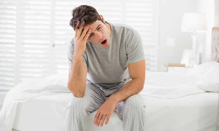 Man with sleep apnea yawns after waking up with a headache and sleepiness