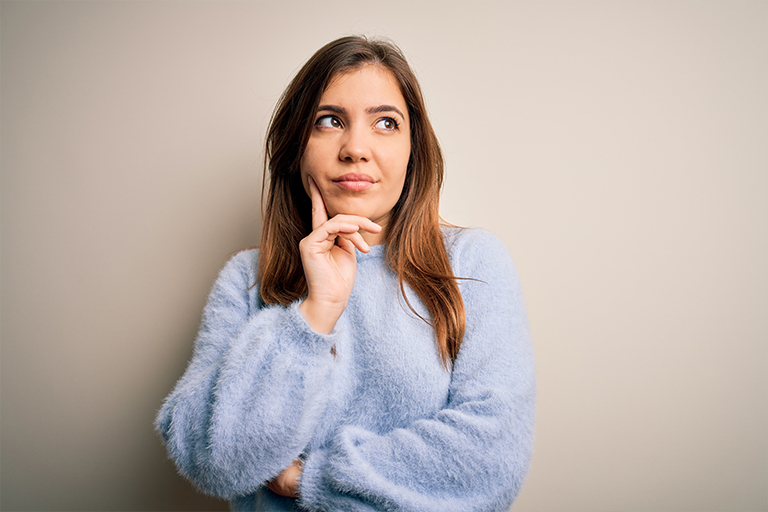 Blonde woman in mint sweater bites her lip and wonders about oral cancer symptoms